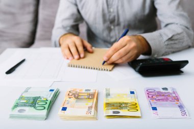 Euro banknotlar istiflenir. Adam muhasebesini yapıyor. Küçük bir işletmede giderlerin dağıtımı. Tasarruf, mevduat, borç verme ve faiz oranı.