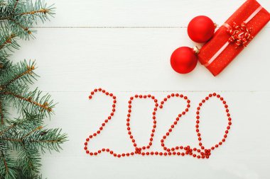 2020 harfli. Yılbaşı kutlaması için kırmızı hediye kutularından, köknar dallarından, beyaz ahşap zeminli balolardan oluşan yeni yıl kutlaması motifleri. Noel zamanını ve kışı düşünün. Düz yatıyordu.