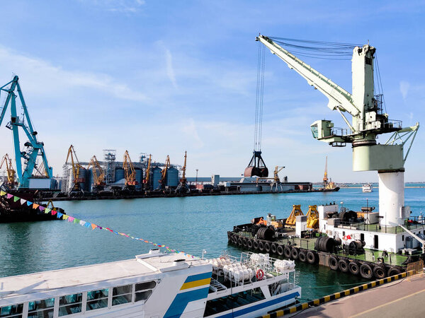Floating cargo crane with a ladle in the seaport over the sea and Granary elevators, Tugboat assist, boats and cranes. Industrial scenery of the sea cargo port, harbor. Excavator on floating platform.