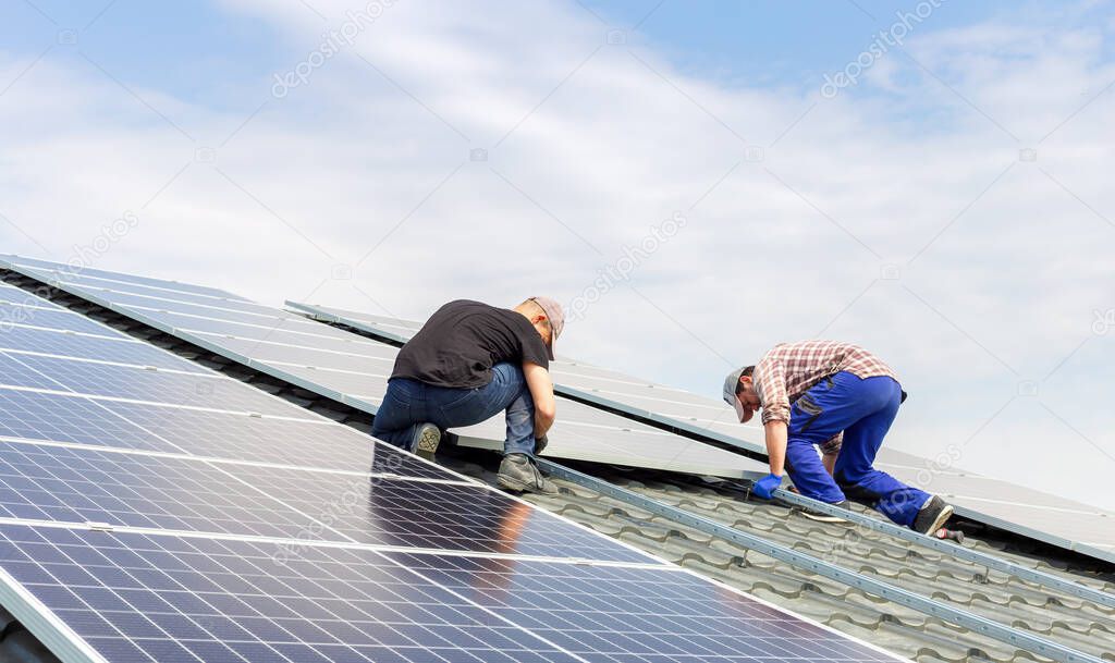 Electrical engineers mans are working installing solar panels on solar station on house roof against blue sky. Building a solar station. Alternative energy ecological concept.