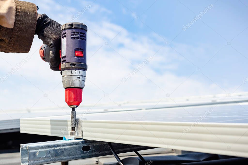 Solar engineer male hand working with drill installing solar panel on house roof against blue sky. Solar energy power. Sun electricity technology. Stock photo solar panels with copy space