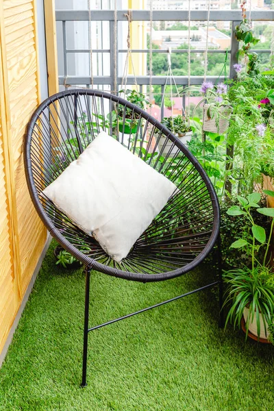 Garden chair with pillow on balcony at home in appartment on lawn grass with house plants flowers. Garden veranda modern terrace. Home gardening, houseplants.Rest relaxation place green oasis in city.