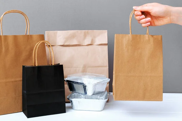 Food delivery service. Brown craft paper bag package in female hand. Delivery mock up packaging. Food foil containers and different paper packages for takeaway food. Mock up.