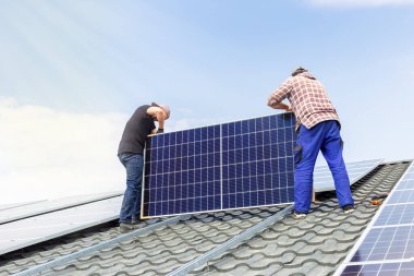 Elektrik mühendisleri güneş panellerini güneşli bir günde mavi gökyüzüne karşı evlerin çatısına kuruyor. Alternatif enerji teknolojisinin geliştirilmesi. Ekolojik kavram