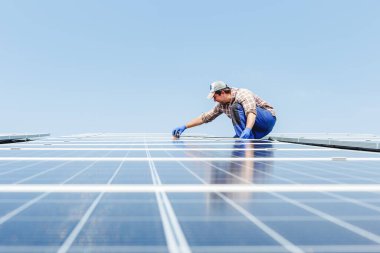 Güneş paneli enerjisi. Elektrik mühendisi çatıdaki güneş istasyonunda mavi gökyüzüne karşı ekipman kullanarak çalışıyor. Alternatif enerji teknolojisinin geliştirilmesi. Ekolojik kavram