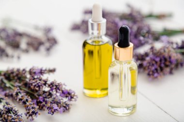 Lavanta esanslı cam şişeler, serum, beyaz ahşap masa üzerine damlatan taze lavanta çiçekleri. Aromaterapi tedavisi, doğal kaplıca ürünleri, eczacı lavanta bitkisi.