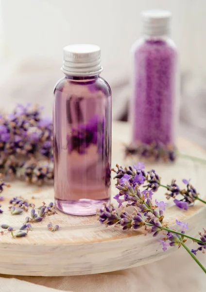 Lavender bath cosmetics products in bottles on white wooden rustic board, fresh lavender flowers, candle, soap, bath beads, Lavender essential oil, natural spa products. Aromatherapy treatment.