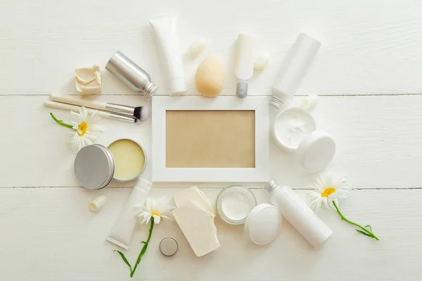 White frame set cosmetic products in white mockup packaging on wooden table flowers, cosmetic bag. Beauty skin care hair treatment cosmetic moisturizer cream body butter soap. Flat lay copy space.