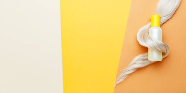 Şampuan şişesi ipliği turuncu renkli arka planda sarı saç bukleleri. Sarı şampuan şişesi. Web uzunluğunda düz pankart kopyalama alanı. Saç bakım kozmetik ürünleri, banyo güzellik ürünleri saç bakımı.