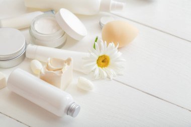 Tahta masaya çiçekli beyaz kozmetik ürünleri koyun. Güzellik süngeri makyaj cilt tedavisi kozmetik nemlendirici cilt kremi sabun losyonu şampuanı. Metin için düz metin kopyalama alanı
