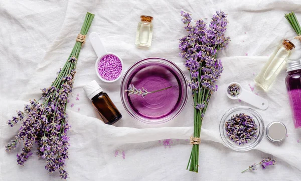 Lavender oils, liquids, parfumes, lavender flowers on white fabric. Set skincare spa beauty cosmetic products. Lavender essential oil. Apothecary herbs for aromatherapy. Flat lay long web banner