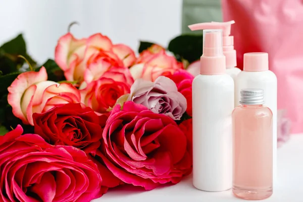Serum, soap, oil on white table floral background. Flower red pink roses natural organic beauty product. Spa, skin care, bath body treatment. Set of pink plastic cosmetic bottles with rose Mockup — Stock Photo, Image