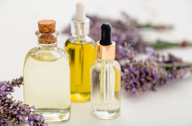 Lavanta yağı şişeleri, serum, beyaz ahşap masa üzerine damlatan taze lavanta çiçekleri. Aromaterapi tedavisi, doğal spa kozmetik ürünleri, eczacı lavanta bitkisi. Cilt kılı kozmetiği.