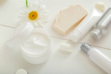 Beyaz kavanozdaki nemlendirici krem ve papatya çiçekleri beyaz cilt ürünlerini tüpler ve şişelere koyuyor. Nemlendirici cilt kremi için taklit beyaz plastik kavanoz, beyaz arka planda losyon.