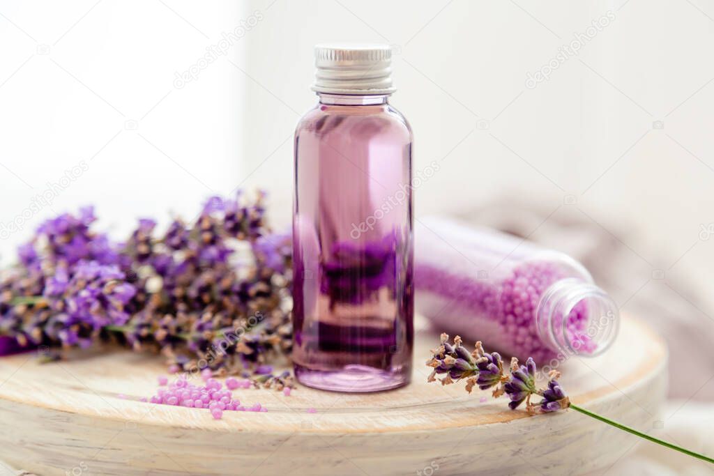 Lavender liquid. Bath cosmetics products in bottles on white wooden rustic board, fresh lavender flowers, soap, bath beads. Lavender essential oil, natural spa products. Aromatherapy treatment