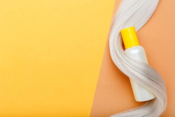 Szampon butelka makieta kosmyk na loki blond włosy na pomarańczowym tle. Żółta butelka szamponu. Kosmetyki do pielęgnacji włosów kosmetyki kąpiel kosmetyki leczenie włosów — Zdjęcie stockowe
