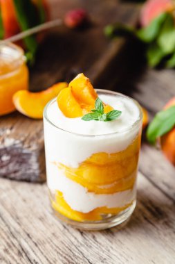 Şeftali meyveli tatlı, cam bardakta, ahşap masada. Meyveli ev yapımı tatlı. Yoğurtlu veya ekşi kremalı meyve salatası.