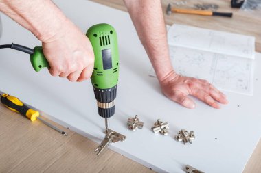 Matkap kullanarak mobilya montajı. Erkek el ustası evdeki aletleri kullanarak mobilya topluyor. Taşınma, ev dekorasyonu, mobilya tamiri ve yenileme