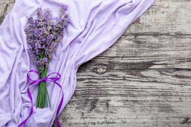 Menekşe kumaşın üzerindeki eski ahşap masa üzerinde taze lavanta çiçeği buketi. Bir demet lavanta. Kurdeleyle tutturulmuş. Kopya alanı da metin için. Flatlay mor bitkisel çiçek çiçeği. Lavanta aromaterapisi