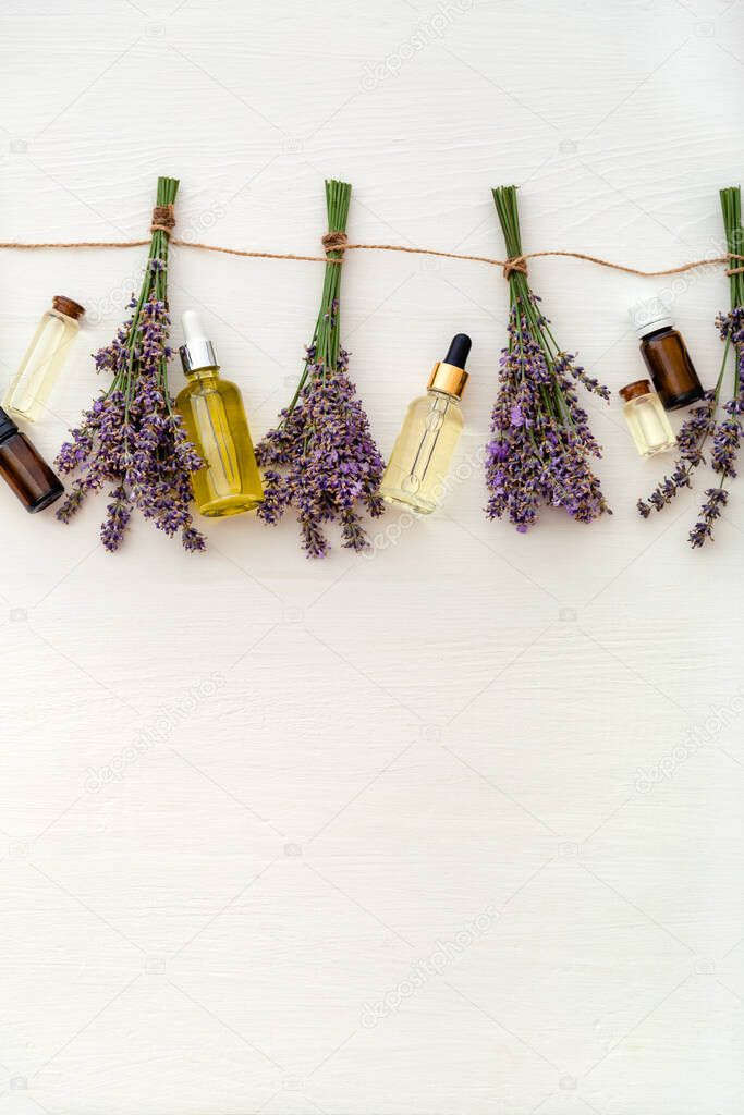 Lavender oil serum with fresh lavender flower bouquets are drying on white wooden background. Lavender essential oil, massage liquid. Flat lay medical apothecary herbs. Skincare spa beauty products.