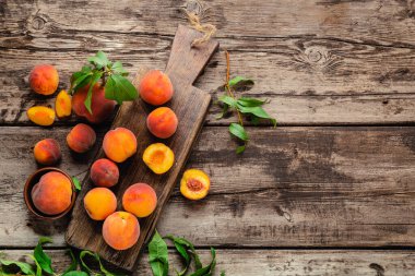 Koyu ahşap tahtada yaprakları olan şeftalili şeftali. Yemek için sulu şeftali hasadı içeren kompozisyon. Taze organik meyve eski ahşap masanın üzerinde duruyordu. Üst görünüm kopyalama alanı.