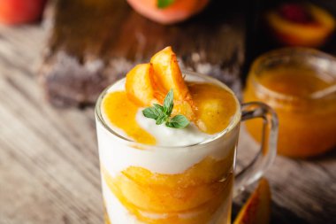 Şeftali meyveli tatlı, cam bardakta, ahşap masada. Meyveli ev yapımı tatlı. Yoğurtlu ya da ekşi kremalı meyve salatası. Kapat..