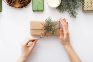 Kadın eli, Noel hediyeli bir kutuyu beyaz masada Noel süslemeleri ile birlikte tutuyor. Noel, Noel, Noel, kış, yeni yıl, sıfır atık kavramı. Düz konum, üst görünüm, kopyalama alanı, arkaplan.