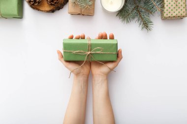 Kadın eli, Noel hediyeli bir kutuyu beyaz masada Noel süslemeleri ile birlikte tutuyor. Noel, Noel, Noel, kış, yeni yıl, sıfır atık kavramı. Düz konum, üst görünüm, kopyalama alanı, arkaplan.