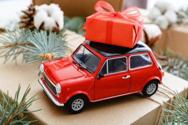 Çatıda kırmızı hediye kutusu olan kırmızı oyuncak araba. Pamuklu Noel arkaplanı, köknar dalları, köknar kozalakları. Noel tatili, kutlama, Noel, Noel, kış, yeni yıl konsepti.