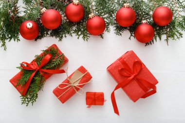 Kırmızı Noel hediyelerinden, kırmızı süslemelerden, beyaz ahşap masa arkaplanındaki köknar dallarından oluşan Noel kompozisyonu. Noel, Noel, kış, yeni yıl konsepti. Düz konum, üst görünüm, kopyalama alanı