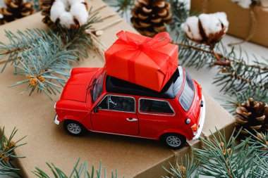 Çatıda kırmızı hediye kutusu olan kırmızı oyuncak araba. Pamuklu Noel arkaplanı, köknar dalları, köknar kozalakları. Noel tatili, kutlama, Noel, Noel, kış, yeni yıl konsepti.