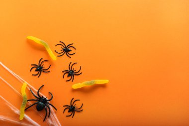 Cadılar Bayramı arkaplanda şeker solucanı, örümcek ağı ve turuncu arka planda Cadılar Bayramı sembolü olarak örümcekler var. Mutlu Cadılar Bayramı konsepti. Kopyalama alanı olan üst görünüm.