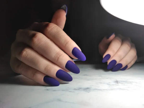 Matte blauwe gel Polish op donkere achtergrond onder lamp — Stockfoto