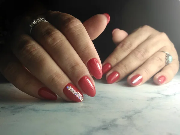 Cute manicure with red coating and rhinestones. Bright red gel polish with a strip of silver rhinestones with sequins.