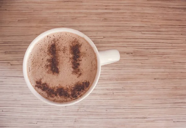 A mug of cappuccino with cinnamon for breakfast. Cinnamon powder in the form of a smiley face on coffee foam. Morning cup of coffee with hot cappuccino. The view from the top.