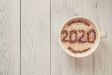 Kahvaltı için bir kupa kapuçino ve tarçın. Kahve köpüğünün üstüne 2020 numara serpiştirilmiş tarçın tozu. Kahve köpüğündeki yeni yılın sembolü. Sabah kahvesi ve sıcak kapuçino..