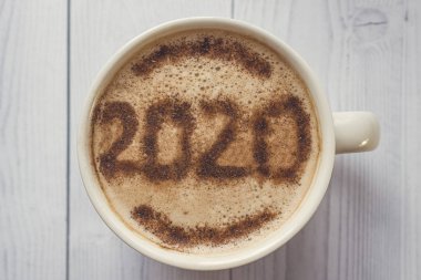 Kahvaltı için bir kupa kapuçino ve tarçın. Kahve köpüğünün üstüne 2020 numara serpiştirilmiş tarçın tozu. Kahve köpüğündeki yeni yılın sembolü. Sabah kahvesi ve sıcak kapuçino..