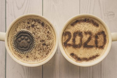 Kahvaltı için bir kupa tarçınlı kapuçino. Tarçın tozu kahve köpüğünün üstüne 2020 numara serpiştirilmiş. Pençe desenli kurabiye kapuçino içinde yüzer. Sabah kahvesi ve sıcak kapuçino.. 