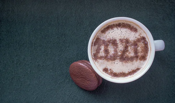 Mug of cappuccino with cinnamon on a dark cyanic background.Cinnamon powder was sprinkled with 2020 figures on coffee foam.Symbol of New year in a cup on coffee foam on woolen fabric.