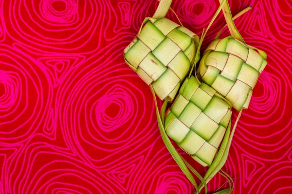 Ketupat Pouches on a red patterned background. Ketupat is a type of dumpling made from rice packed inside a diamond-shaped container of woven palm leaf pouch.