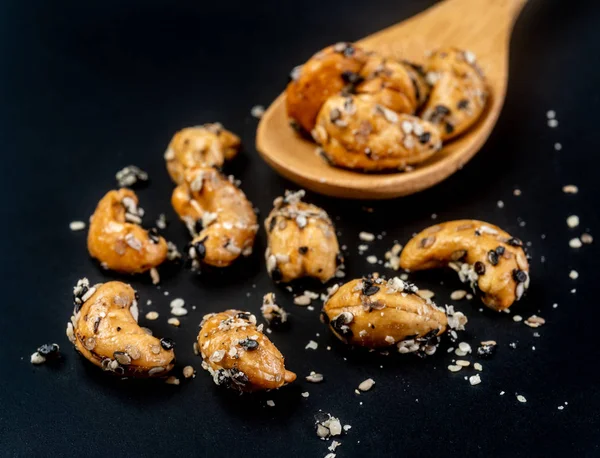 Sesam gecoate cashewnoten op houten lepel. Geïsoleerd op zwarte BAC — Stockfoto