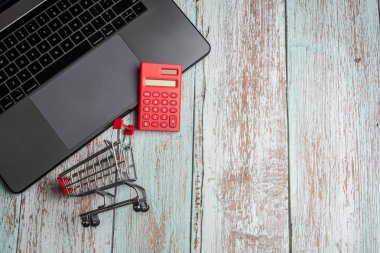 Ahşap masada dizüstü bilgisayar, hesap makinesi ve alışveriş sepeti. Online sho