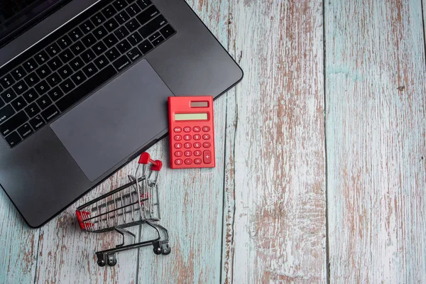 Laptop, calculator and shopping cart on wooden table. Online Sho