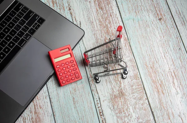 Laptop, calculator and shopping cart on wooden table. Online Sho