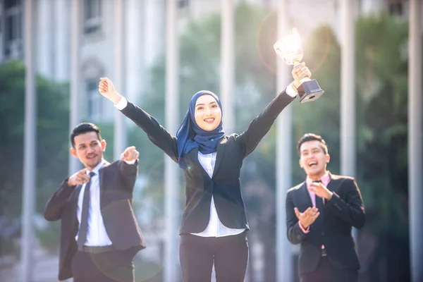 Successful Muslim business woman with arms up holding a trophy a