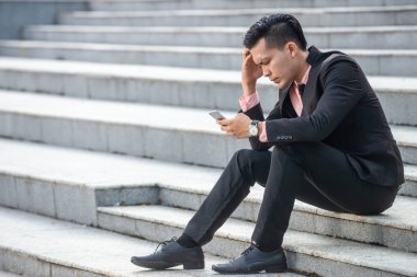 Stresli ve öfkeli Asyalı işadamı akıllı telefon scre bakıyor