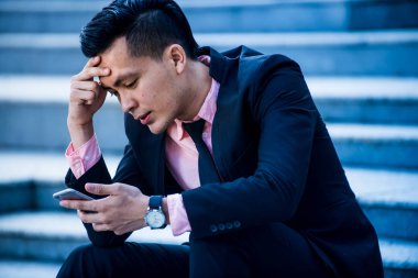 Stresli ve öfkeli Asyalı işadamı akıllı telefon scre bakıyor