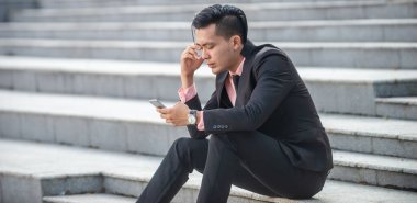 Stresli ve öfkeli Asyalı işadamı akıllı telefon scre bakıyor