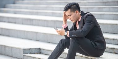 Stresli ve öfkeli Asyalı işadamı akıllı telefon scre bakıyor