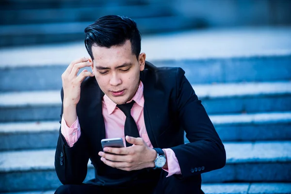 Stressed and angry asian businessman  looking at smartphone scre